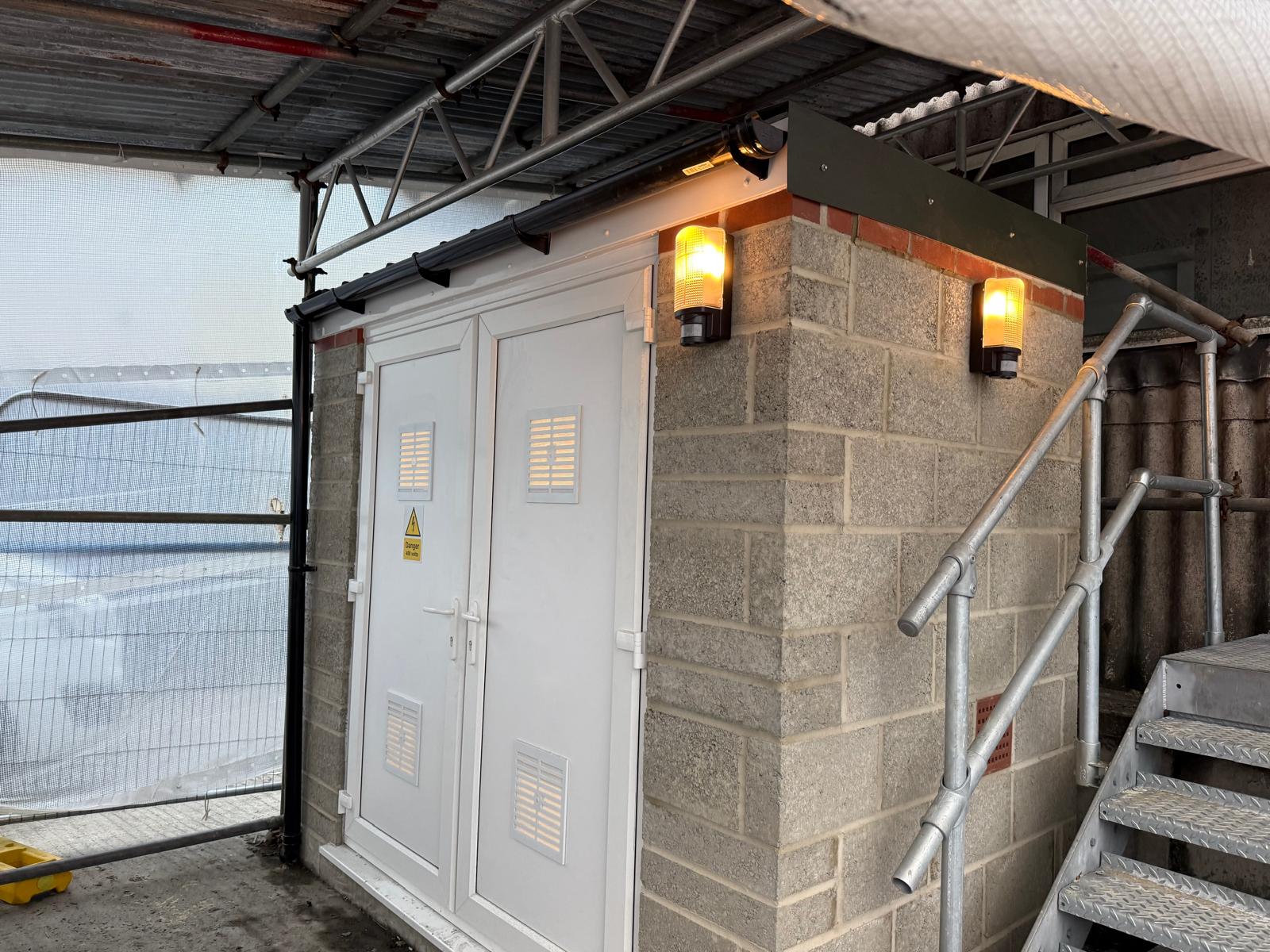 Refitted stone electrical box shed with new doors and outdoor lighting.